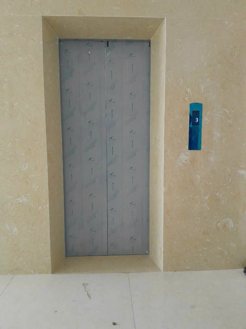 Cửa thang máy màu xám đang lắp đặt trong sảnh tòa nhà với bảng điều khiển tầng bên phải